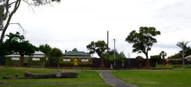 Garden, with houses behind. It appears as if the houses, gum trees and the garden in front are all one scene